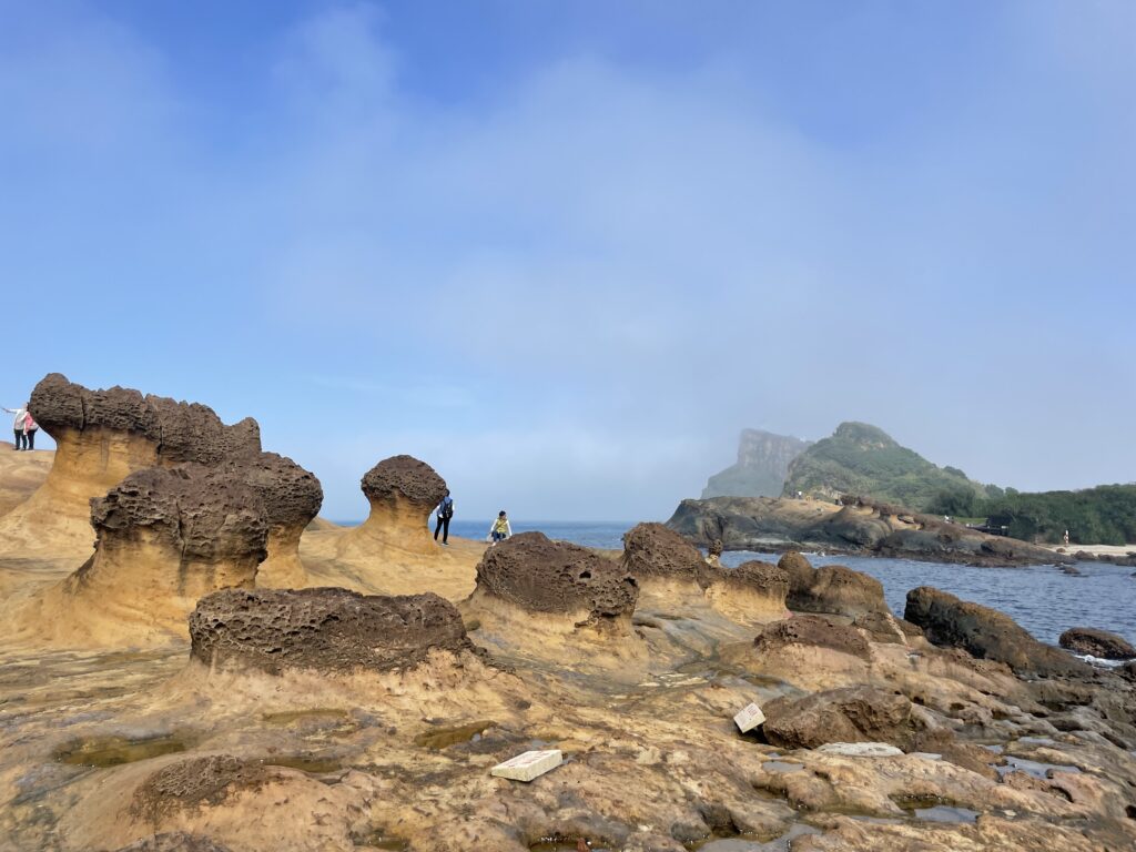 Image shows beautiful rock formations, sea, and green hill at Yehliu Geopark.