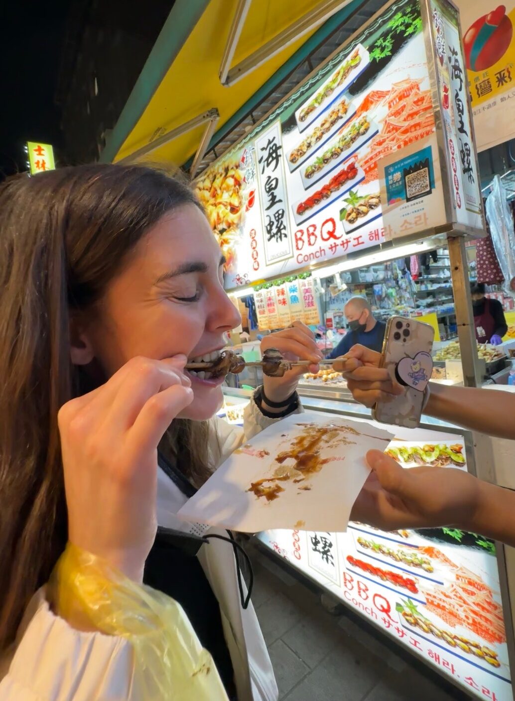 Image of me biting a sea snail skewer at Shilin Night Market.